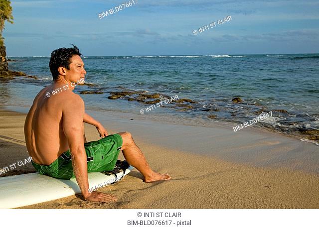 Japanese man sitting on surfboard on beach