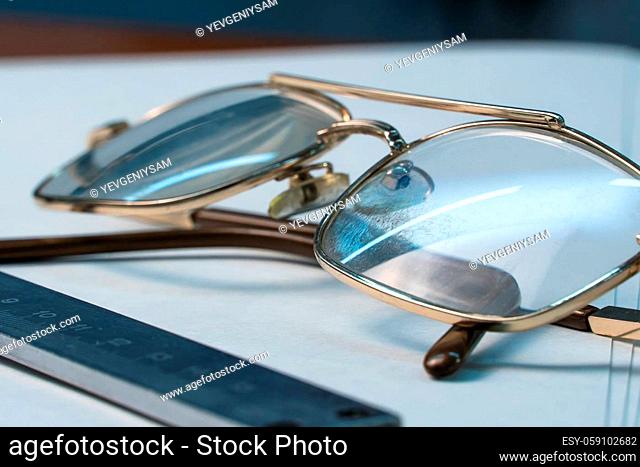 Old eyeglasses and a ruler for drawing lie on the table on a white background. Glasses on the table