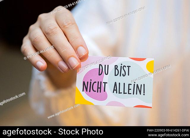 PRODUCTION - 24 August 2022, Berlin: A person holds an Alcoholics Anonymous (AA) business card with the words ""You are not alone"" outside an AA meeting