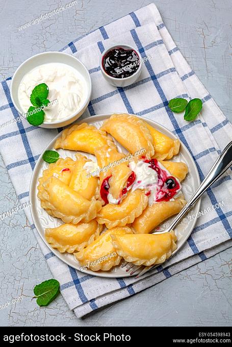 Russian and Ukrainian cuisine - dumplings with cottage cheese served with berry sauce and sour cream. Top view