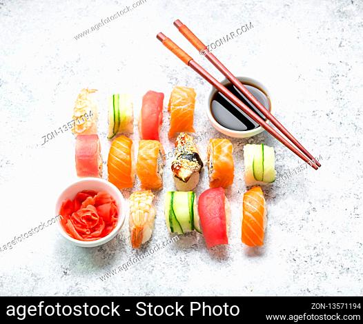 Assorted sushi set on white concrete background. Japanese sushi, rolls, soy sauce, ginger, chopsticks. Top view. Sushi nigiri. Japanese dinner/lunch