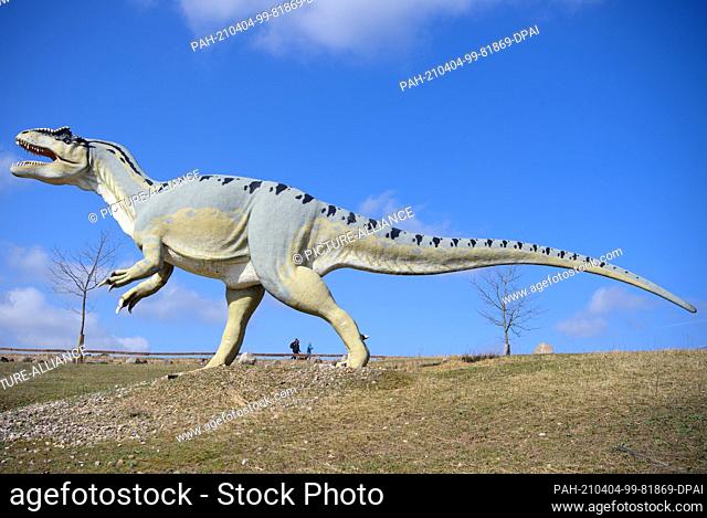 04 April 2021, Brandenburg, Oranienburg/ Ot Germendorf: Visitors to the Animal Leisure and Prehistoric Park walk along behind an Allosaurus in sunny spring...