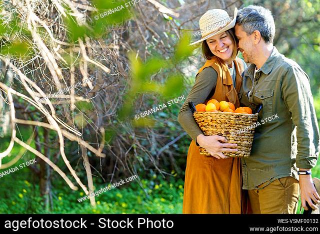 Hapy couple with basket full of oranges in the field