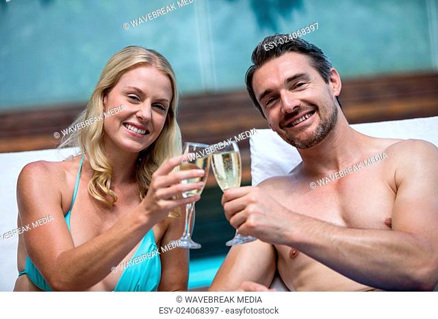 Couple sitting on sun lounger toasting champagne