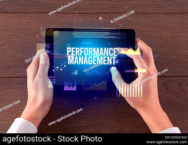 Close-up of hands holding tablet with PERFORMANCE MANAGEMENT inscription, modern business concept