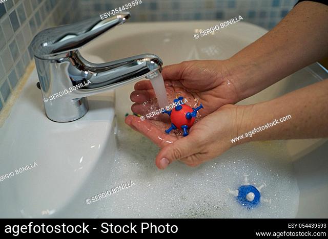 Hands holding models of coronavirus in soapy water to wash