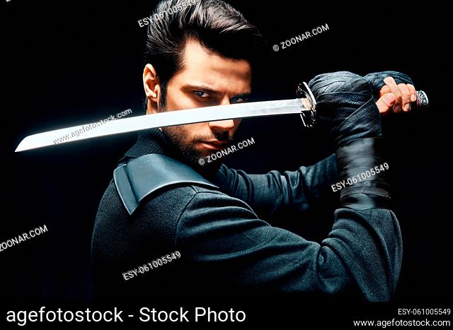 Warrior man posing with a sword ready to stab enemy isolated on black background