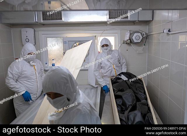 30 May 2020, Turkey, Istanbul: Employees of the Istanbul Municipal Morgue, wearing protective suits and face masks, prepare the body of a man who died of...
