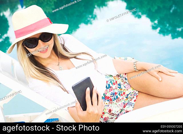 The attractive woman at poolside on vacation is using phone or making selfie about herself