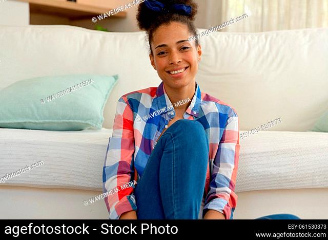 Mixed race woman sitting on the floor looking at camera and smiling at home