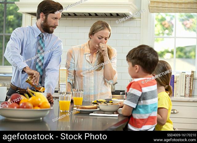 Mom who is feeling under the weather with family in kitchen, struggling to get the kids breakfast and ready to start the day