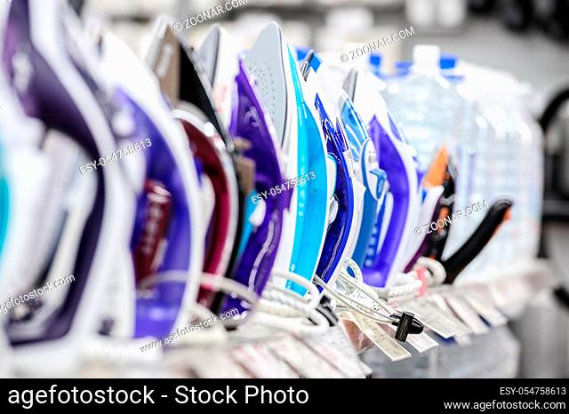 row of colored electric irons at retail store shelf, selective focus