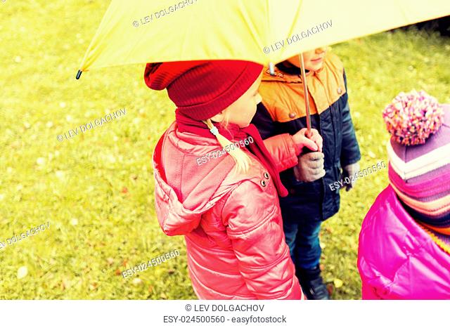 childhood, friendship, season, weather and people concept - close up of kids standing under umbrella in autumn park