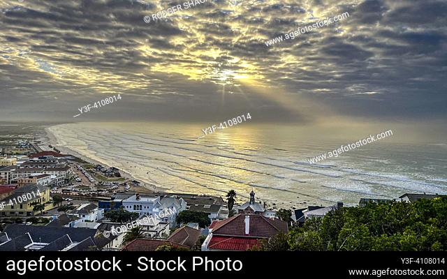 Sun rises over the sea and village of Muizenberg beach and Surfer's Corner