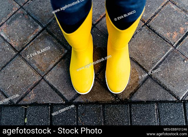 Woman wearing yellow boots standing on street during rainy season