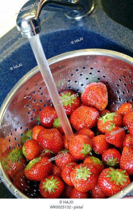 Close-up of strawberries in colander under faucet