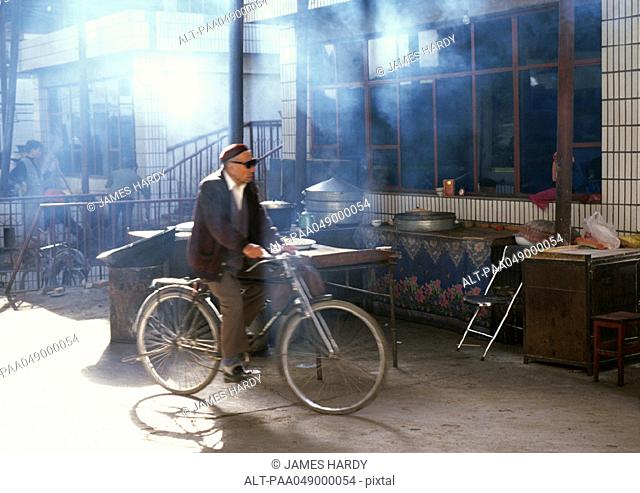 China, Xinjiang Province, Turpan, man riding bicycle near shop front
