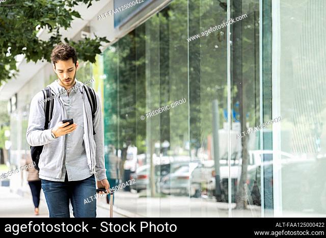 Young man with luggage walking on footpath