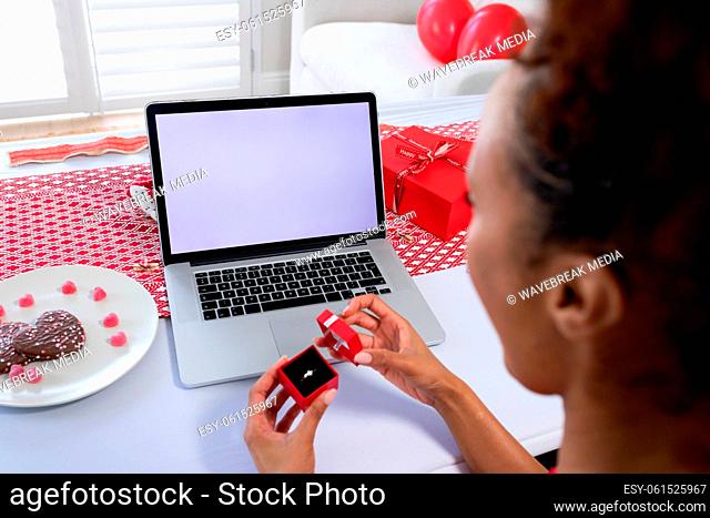 African american woman opening ring box on videocall on laptop at home