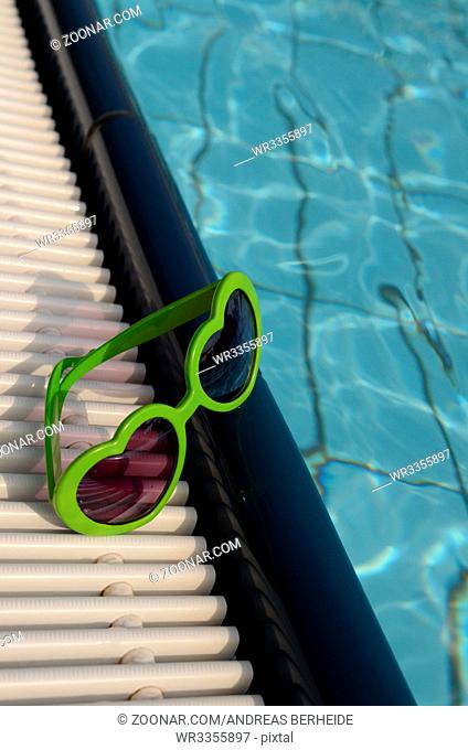 Green sunglasses with heart shapes on a swimming pool