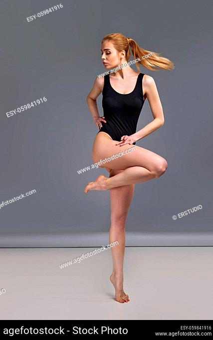 gorgeous slim blonde woman with perfect body in black bodysuit posing on studio background