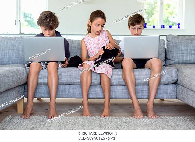 Brothers and sister on sofa with computers and knitting