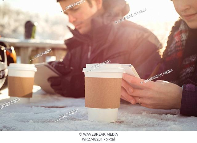 Skier couple using mobile phone and digital tablet at table