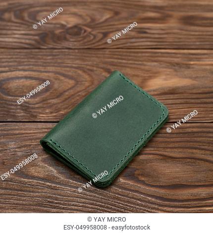 Green two-pocket closed leather handmade cardholder lies on wooden background. Soft focus on background. Stock photo on blurred background