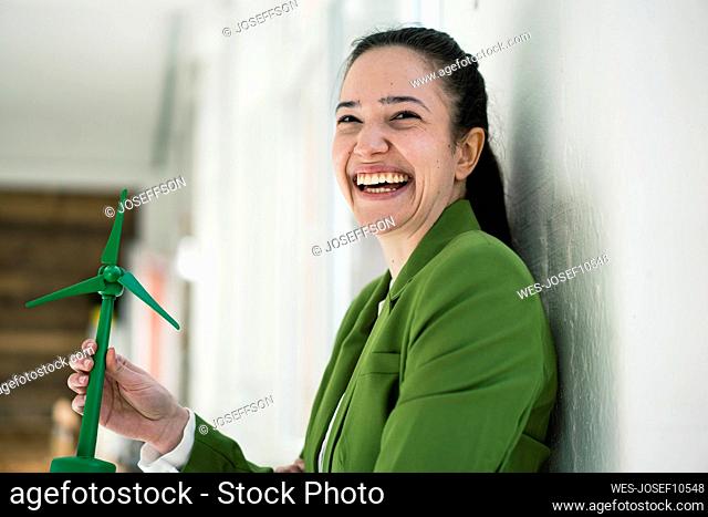 Cheerful businesswoman with wind turbine model by wall