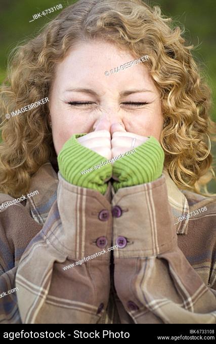 Pretty young woman sneezing outdoors