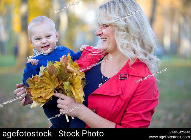 Mom with a toddler on a walk in the autumn park. Beautiful woman holds little son in the arms on the street