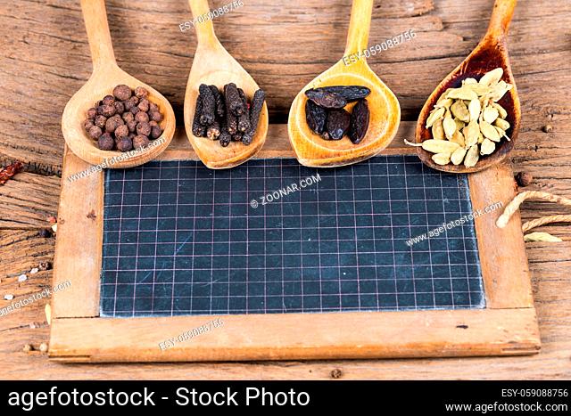 Closeup of four wooden cooking spoons with various exotic spices and an old slate blackboard for labeling on a rustic wooden background