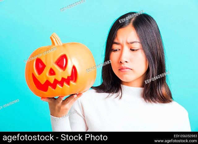 Portrait of Asian beautiful young woman holding orange model pumpkins, funny happy female with ghost pumpkins, studio shot isolated on blue background