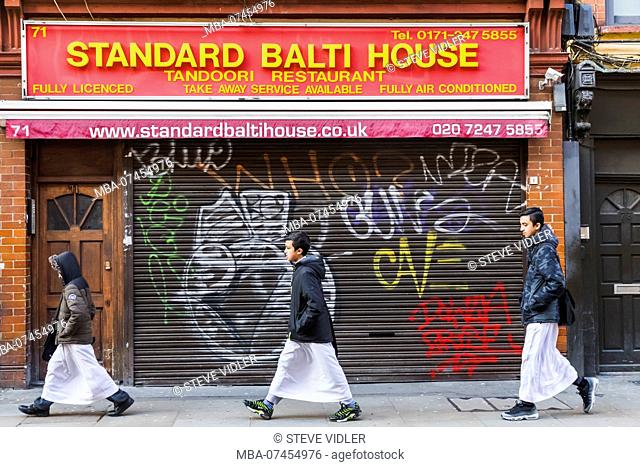 England, London, Shorditch, Brick Lane, Muslim Boys Walking Past Indian Restaurant