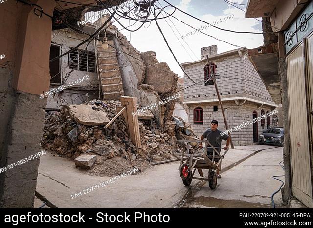 07 July 2022, Iraq, Mosul: A picture made available on 09 July 2022 shows a young man pushing a trolley past the rubble of a destroyed building in the Old City...