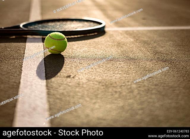 Surface level of tennis ball and racket on white lines at tennis court during sunset, copy space