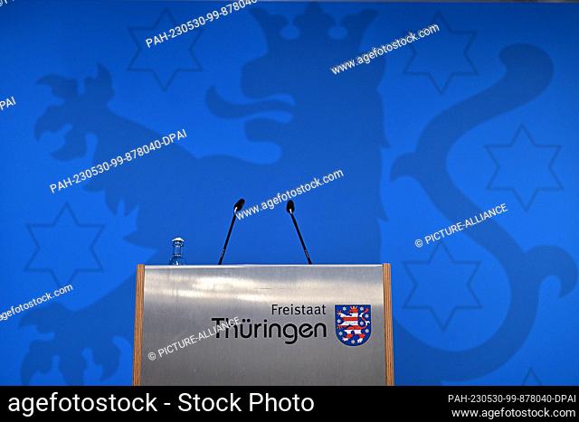 30 May 2023, Thuringia, Erfurt: The lectern with microphones and the inscription ""Free State of Thuringia"" including coat of arms in front of a blue wall with...