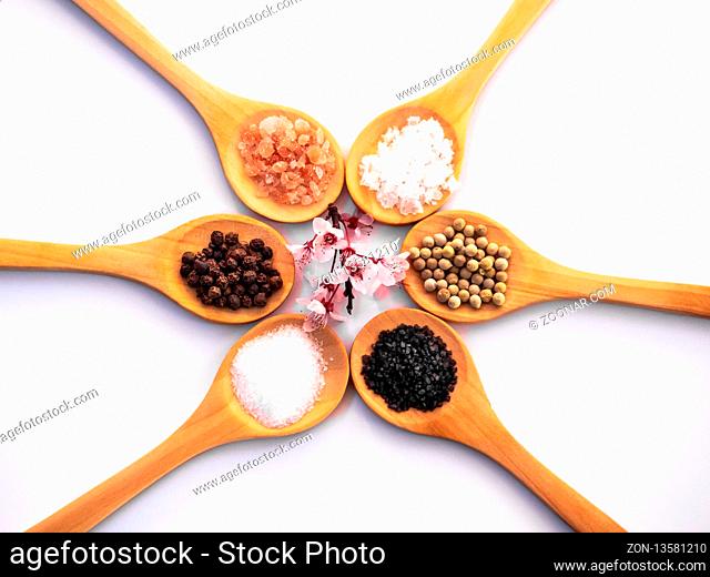 Wooden spoons with himalayan salt, black hawaii salt, common salt, salt flakes and peppercorns on a white background