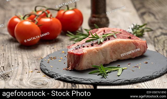 fresh piece of beef, striploin steak on a black board with spices, close up