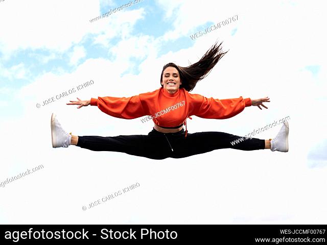 Portrait of beautiful brunette jumping against sky