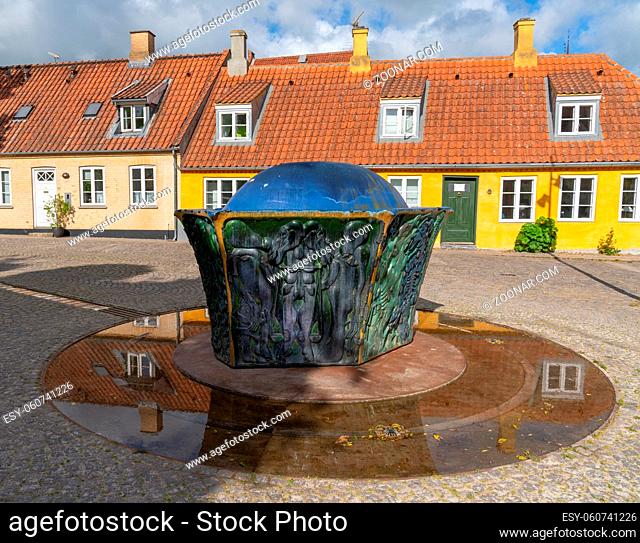 Roskilde, Denmark . 13 June, 2021: colorful sculpture and fountain with reflections and traditional houses in the background
