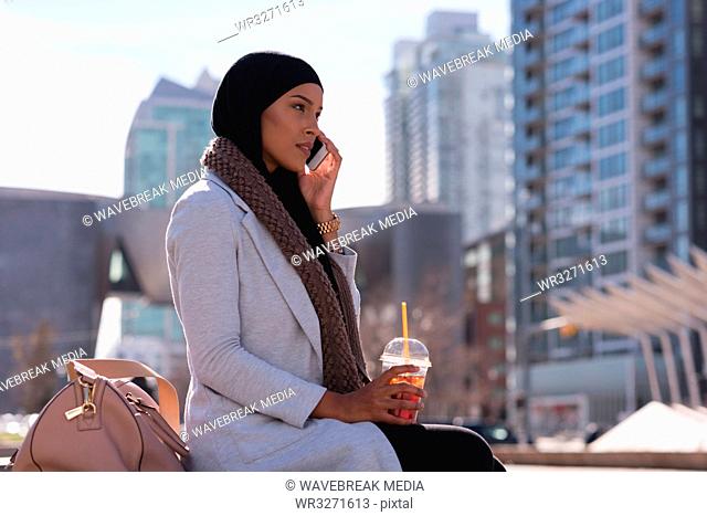 Woman having cold coffee while talking on mobile phone