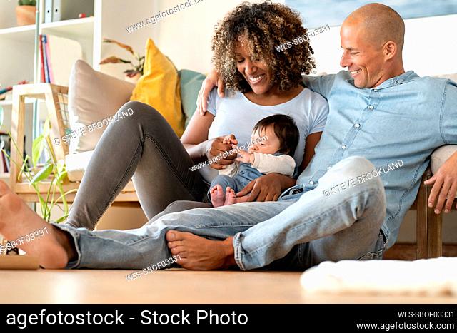 Smiling mother and father looking at baby while sitting on floor at home