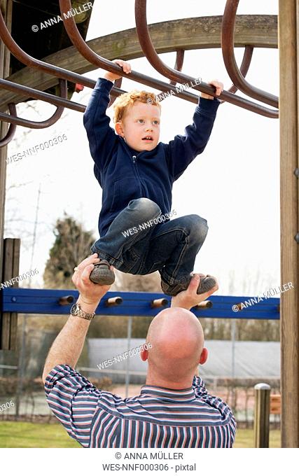 Father helping son on playground climbing on jungle gym