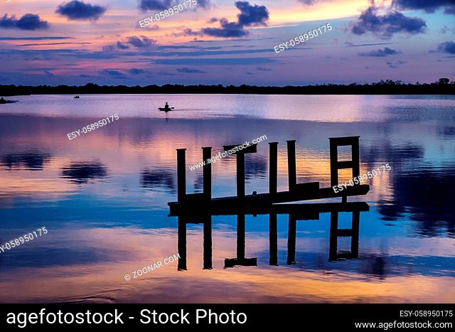 Sunset at a lagoon with Utila letter sign with kanu in background in blue purple colours, Utila, Honduras, Central America