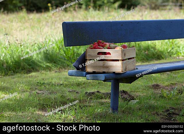 Apples, strawberries and pears in an old wooden crate on a blue bench