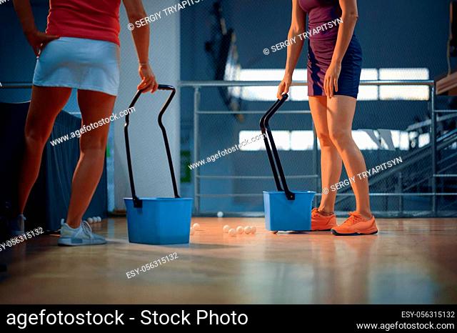 Women with baskets pick up balls after table tennis match, ping pong players. Friends playing table-tennis indoors, sport game with racket and ball