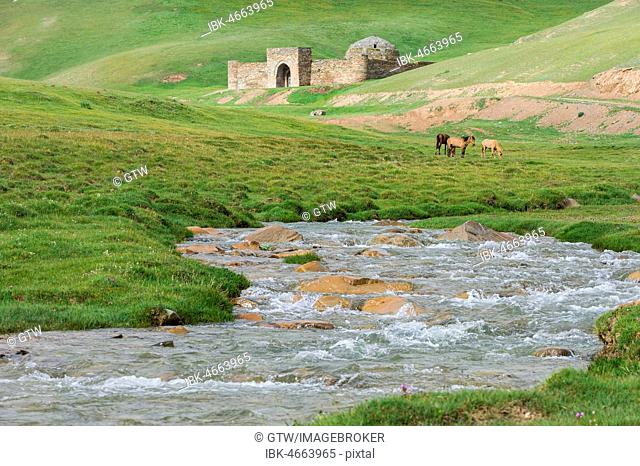 Tash Rabat with horses on meadow and mountain river, 15th century caravanserai, Naryn Province, Kyrgyzstan