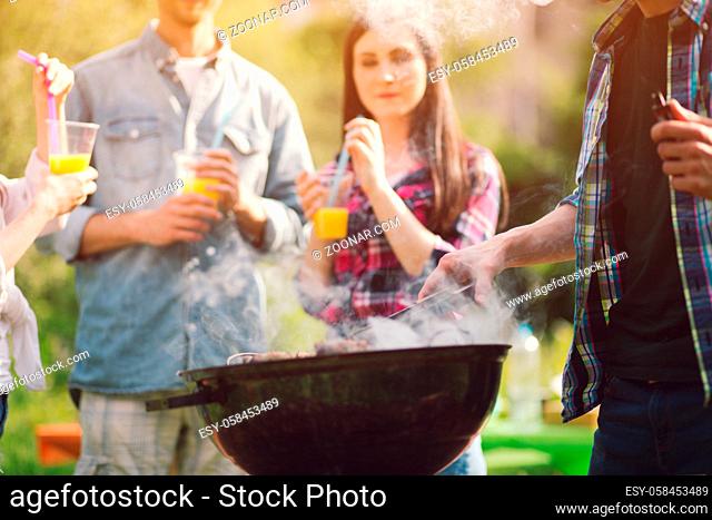 Company of friends spending time together frying meat. Group of friends cooking meat outdoors on grill on warm sunny day while on picnic