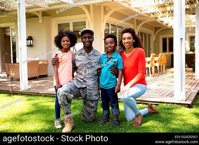 Portrait of a young adult African American male soldier in the garden outside his home, kneeling with his arms around his young son and daughter
